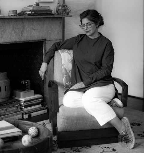 Woman in glasses sits on armchair.