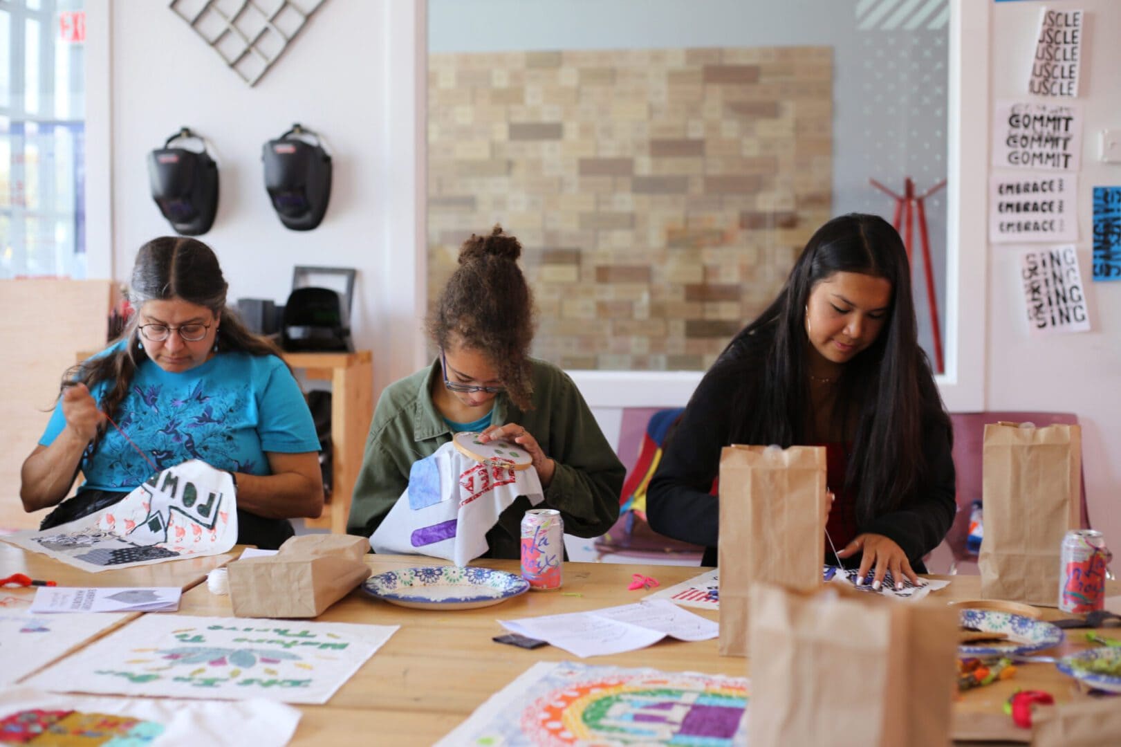 Three women embroidering on fabric at table.