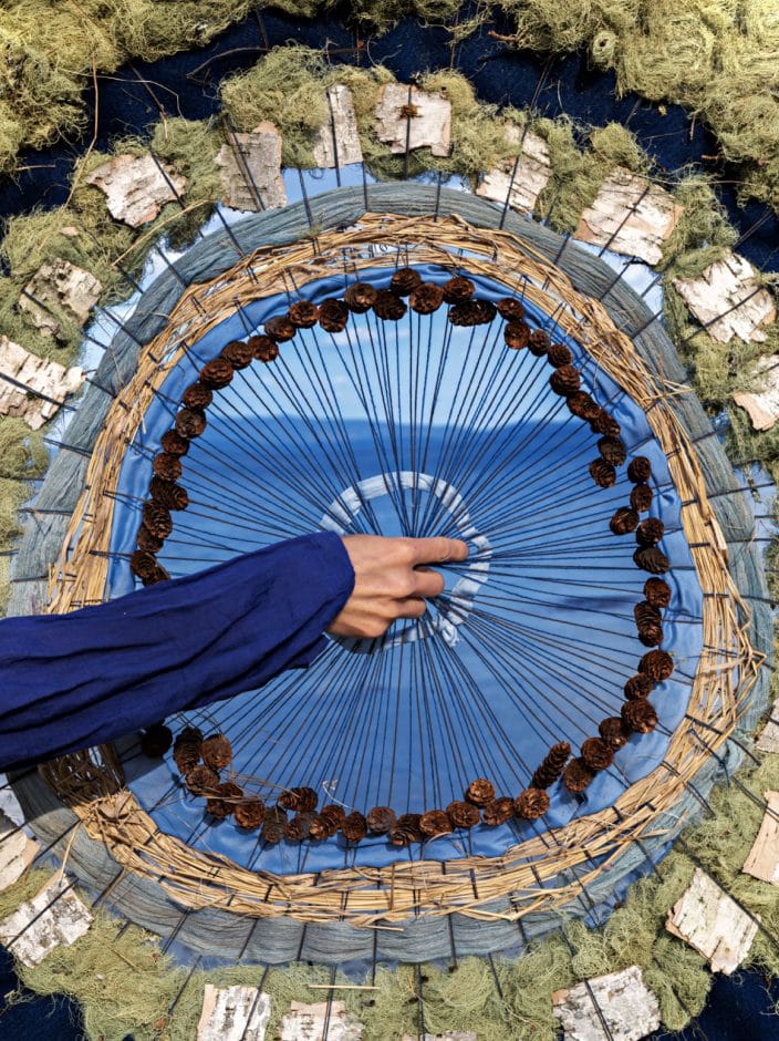 Hand weaving a circular blue tapestry.