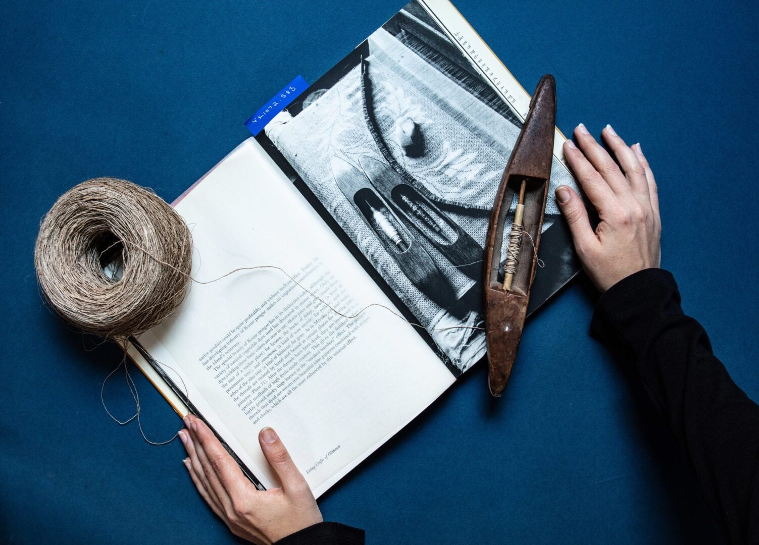 Book with yarn, weaving tools, and hand.