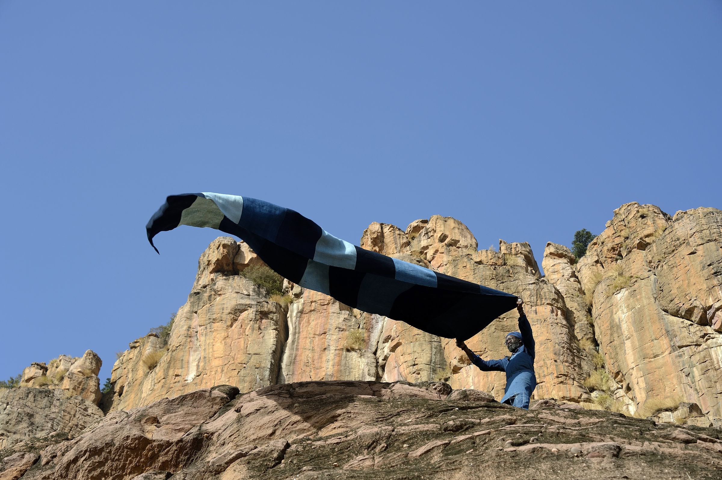 Person holding fabric against rocky cliffs.