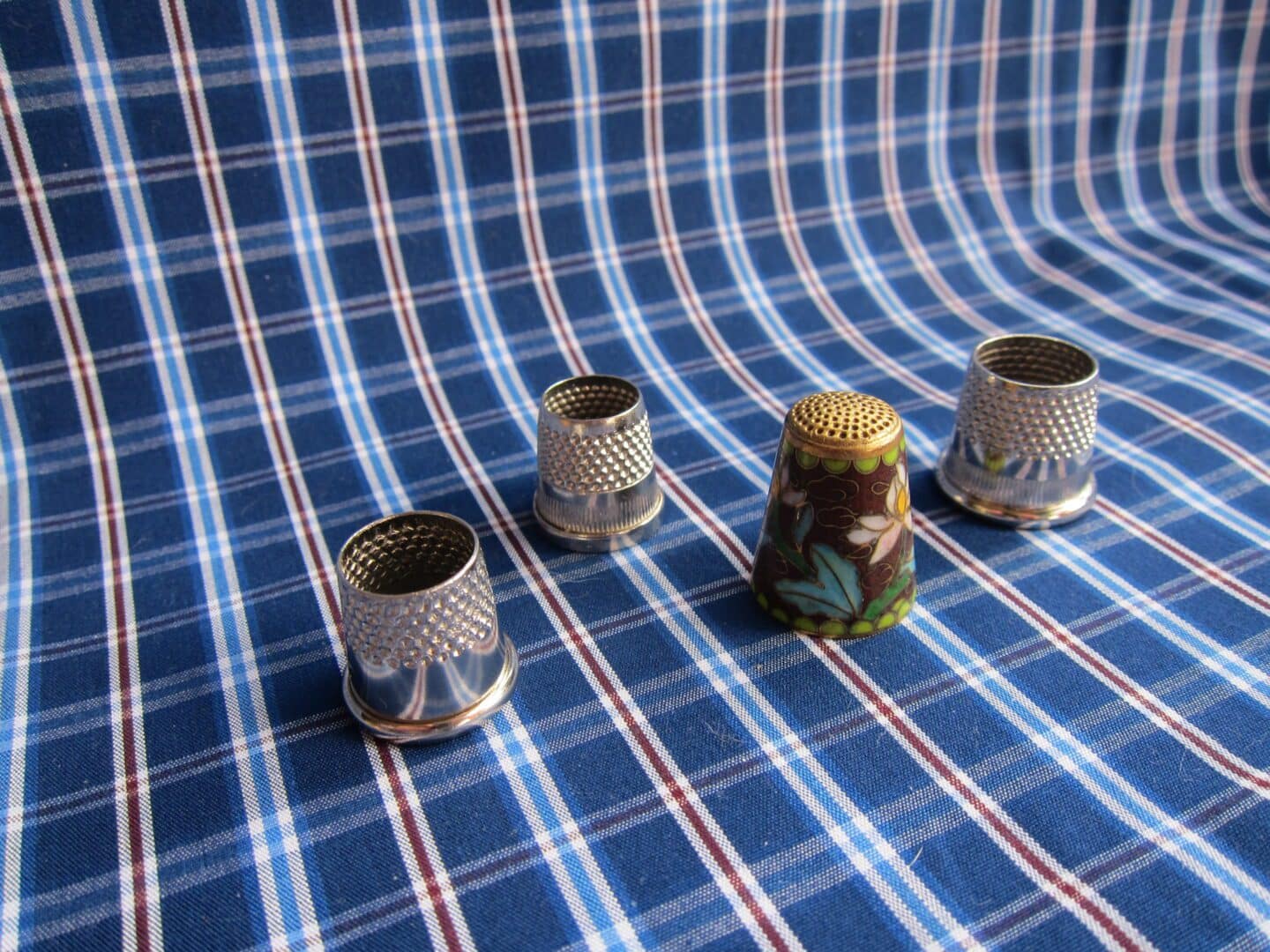 Four thimbles on a blue plaid fabric.