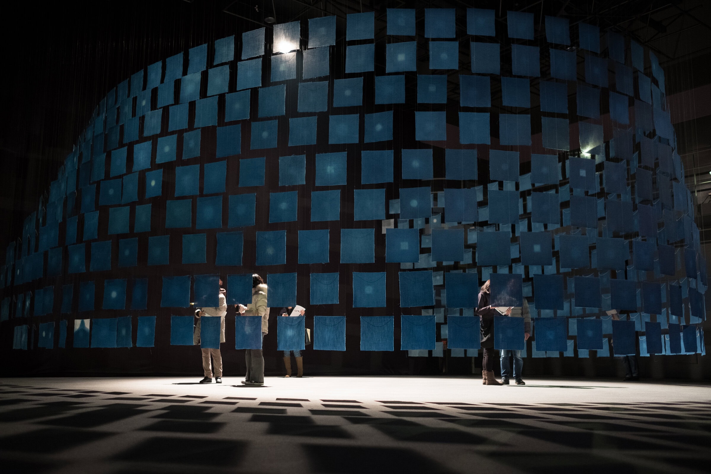 Blue fabric squares hanging in a dark room.