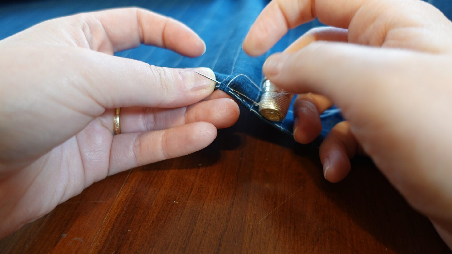 Close-up of hands sewing blue fabric.