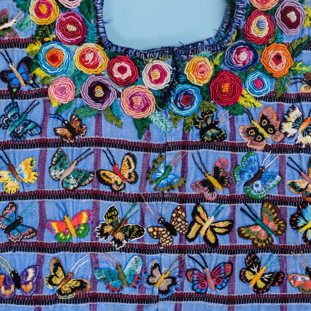 Colorful embroidered butterflies and flowers on blue fabric.