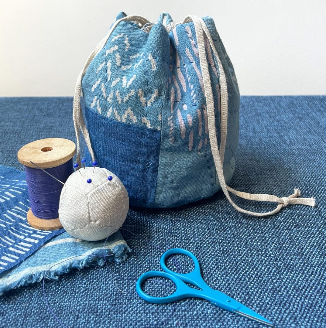 Blue fabric drawstring bag, needle, thread, and scissors.