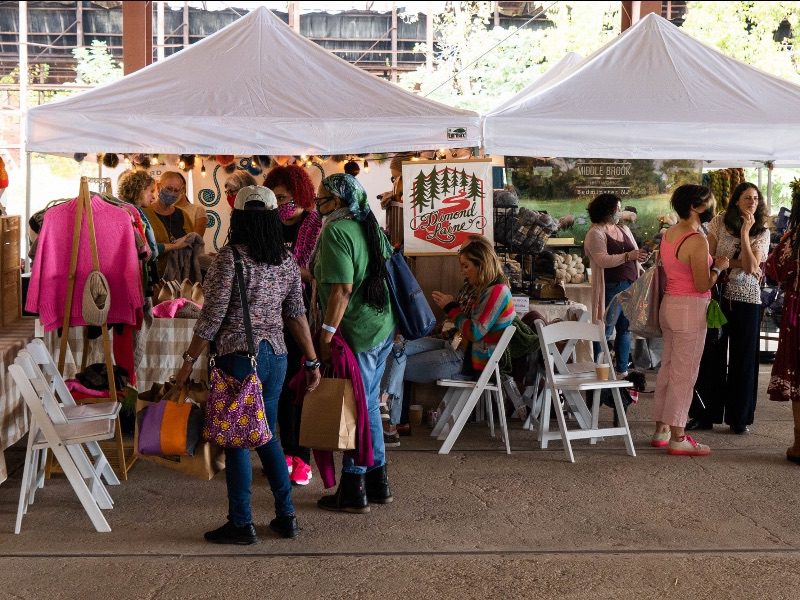 People shop at an outdoor market under tents.