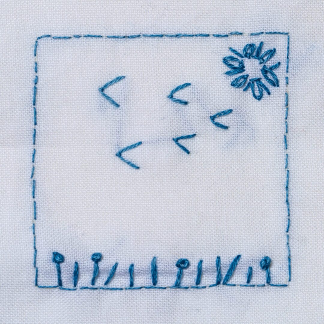 Blue embroidered flower and stems on fabric.