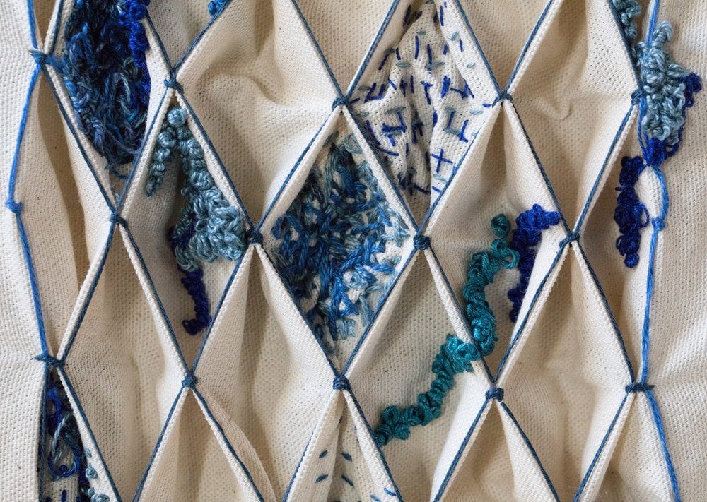 Blue embroidery on white fabric grid.