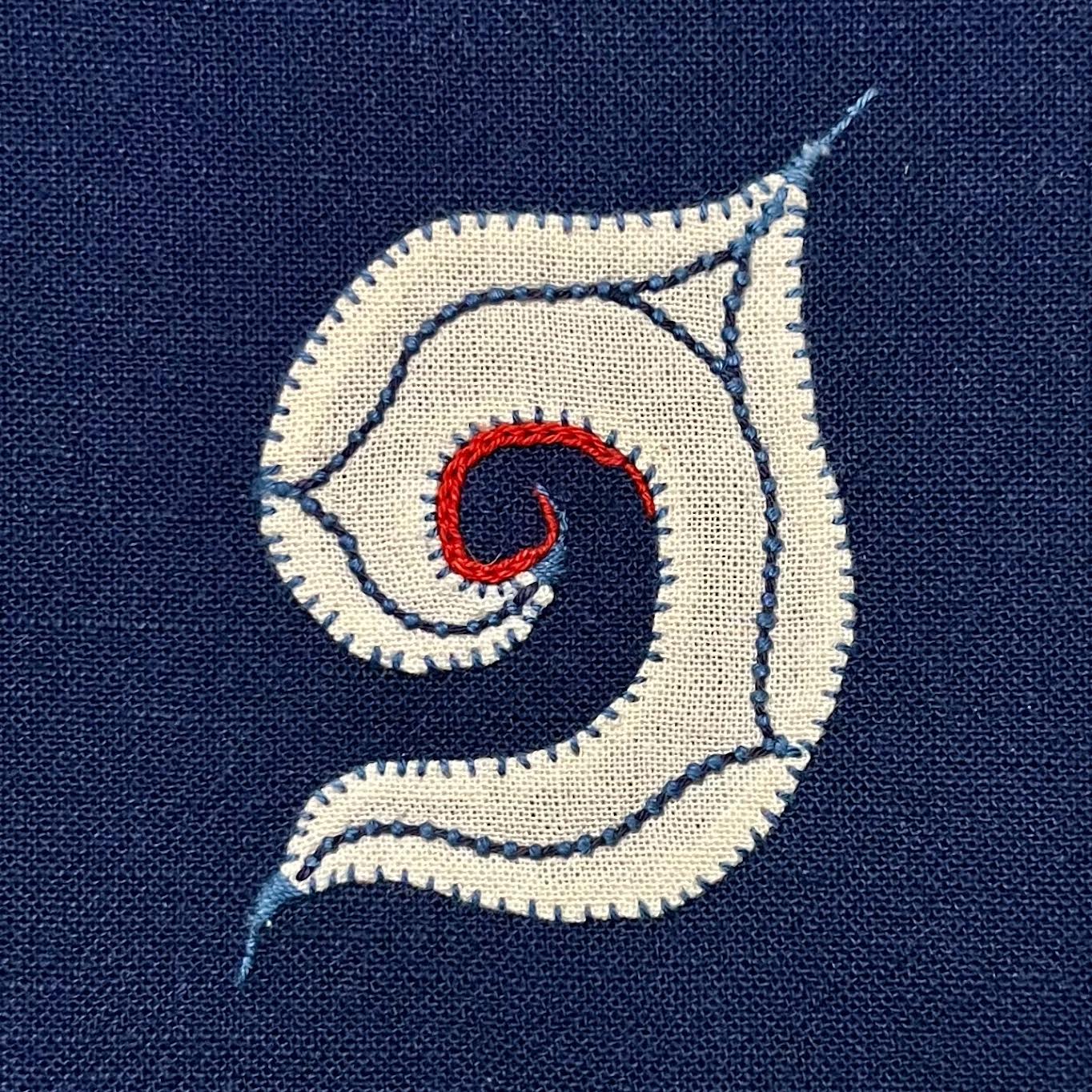 Embroidered letter G on blue fabric.