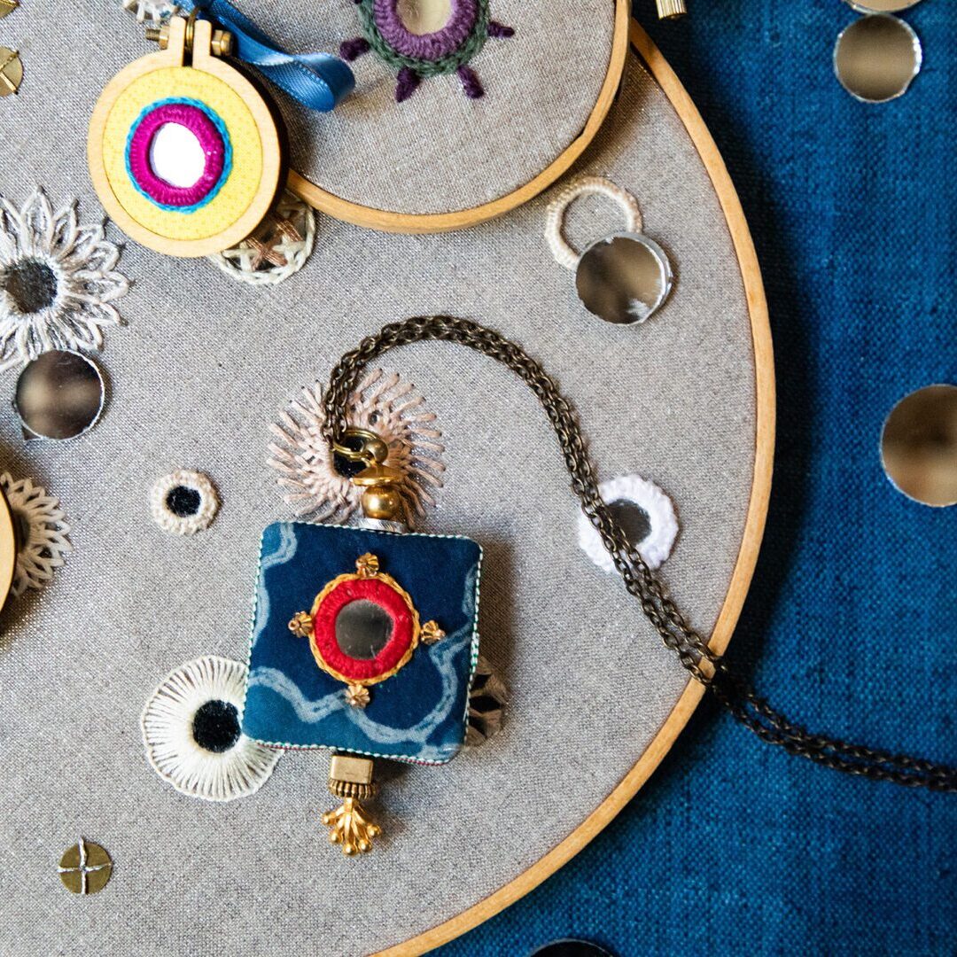 Embroidered pendant with mirror and chain.