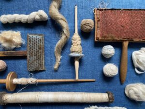 Handspinning tools and yarn on blue fabric.