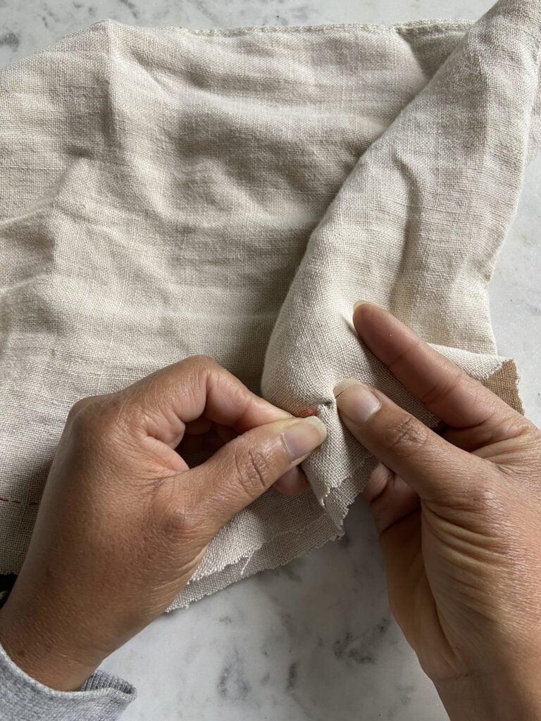 Hand sewing fabric with red thread.