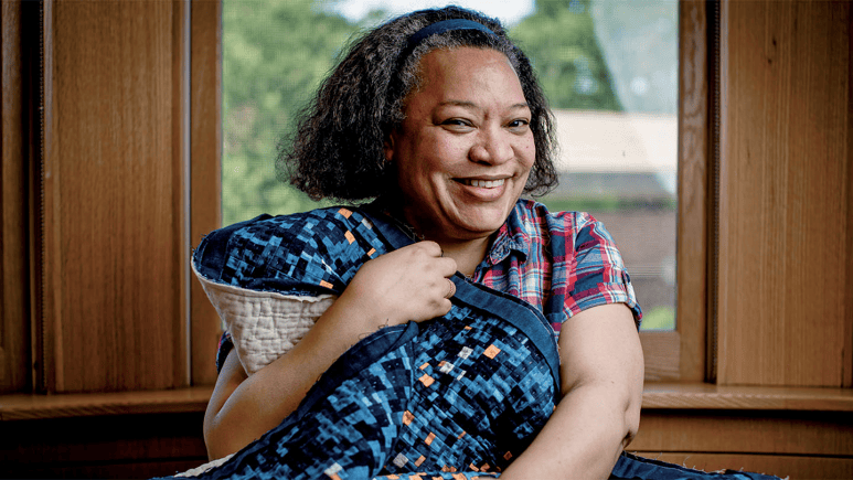 Smiling woman holding a quilt.