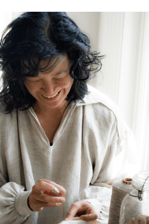 Woman smiling, threading a needle.