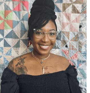 Smiling woman with glasses and a tattoo.