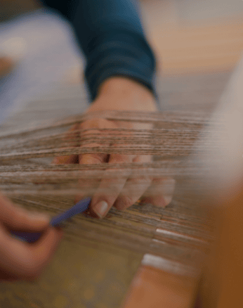 Hand weaving brown yarn on a loom.