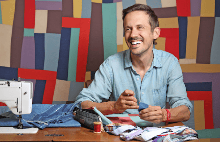 Smiling man sewing with colorful fabric.