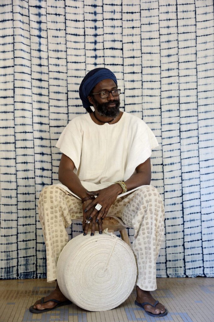 Man in white sitting with fabric roll.