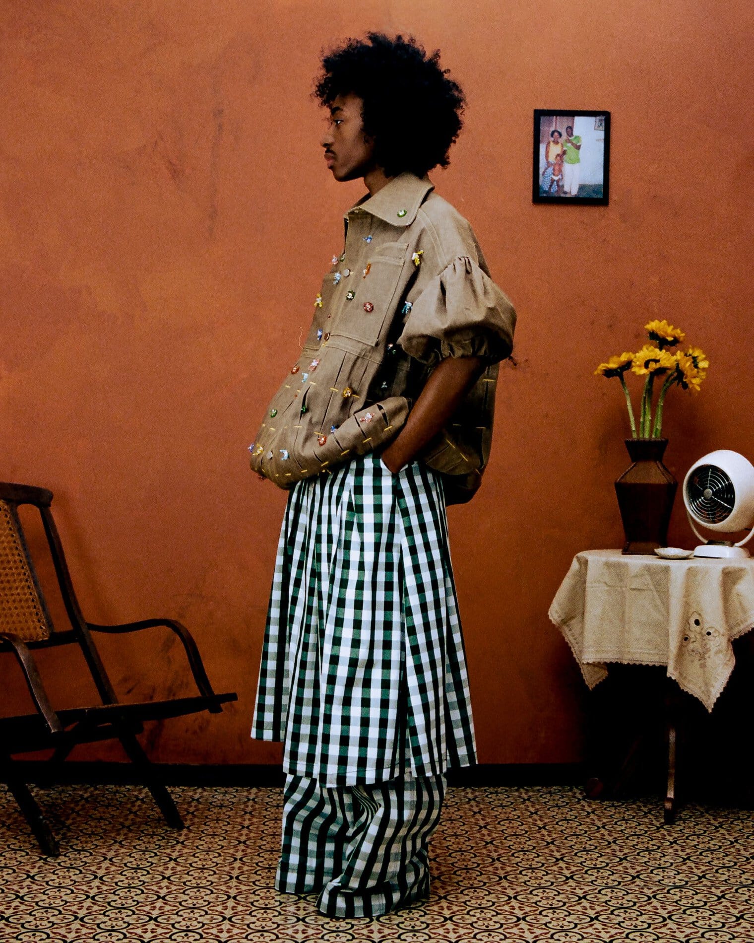A model poses in an oversized puff-sleeved dark khaki jacket with bejeweled embellishments allover, and green-and-white gingham pants and skirt.