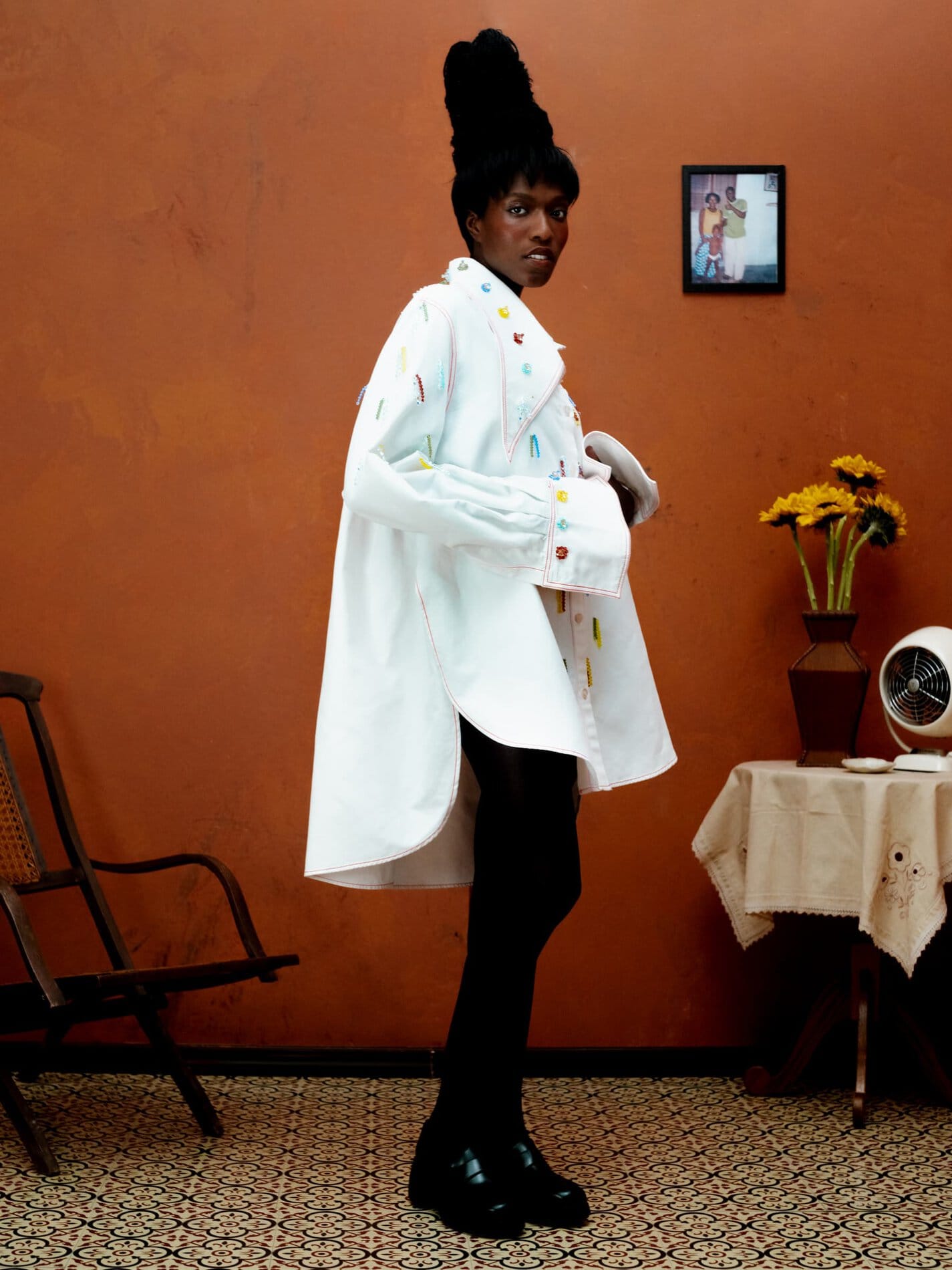 A model poses in an oversized white button down with red contrast stitching and clear, blue, yellow, and green swarovski crystal embellishments.

