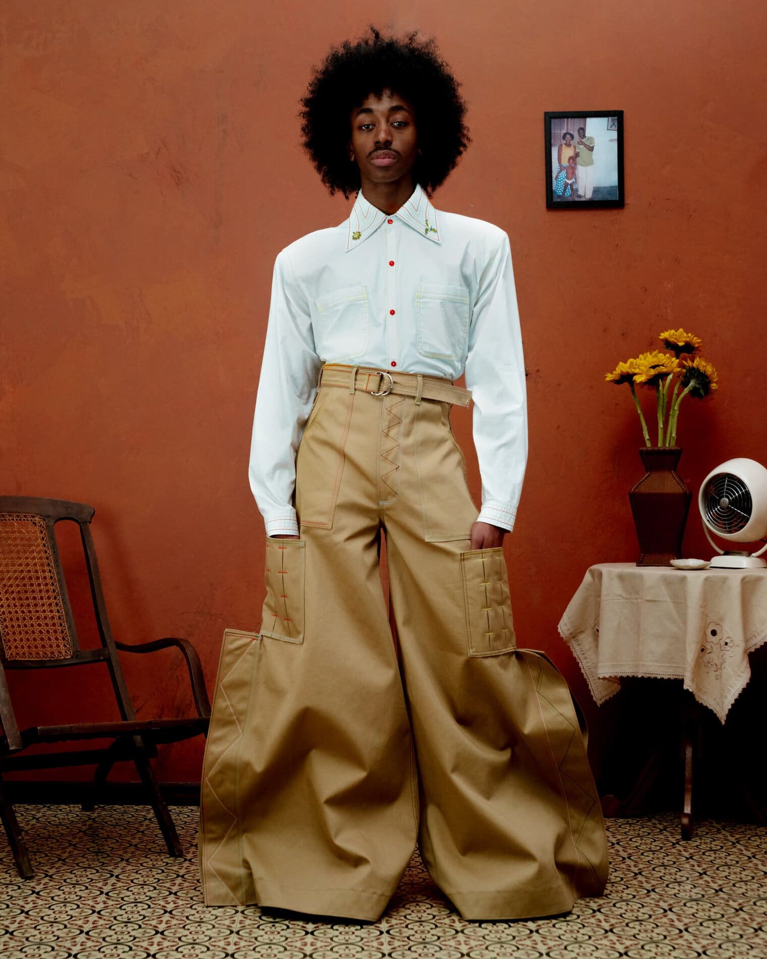 A model poses in a long white button down shirt and high waisted flared cargo pants with contrast stitching.
