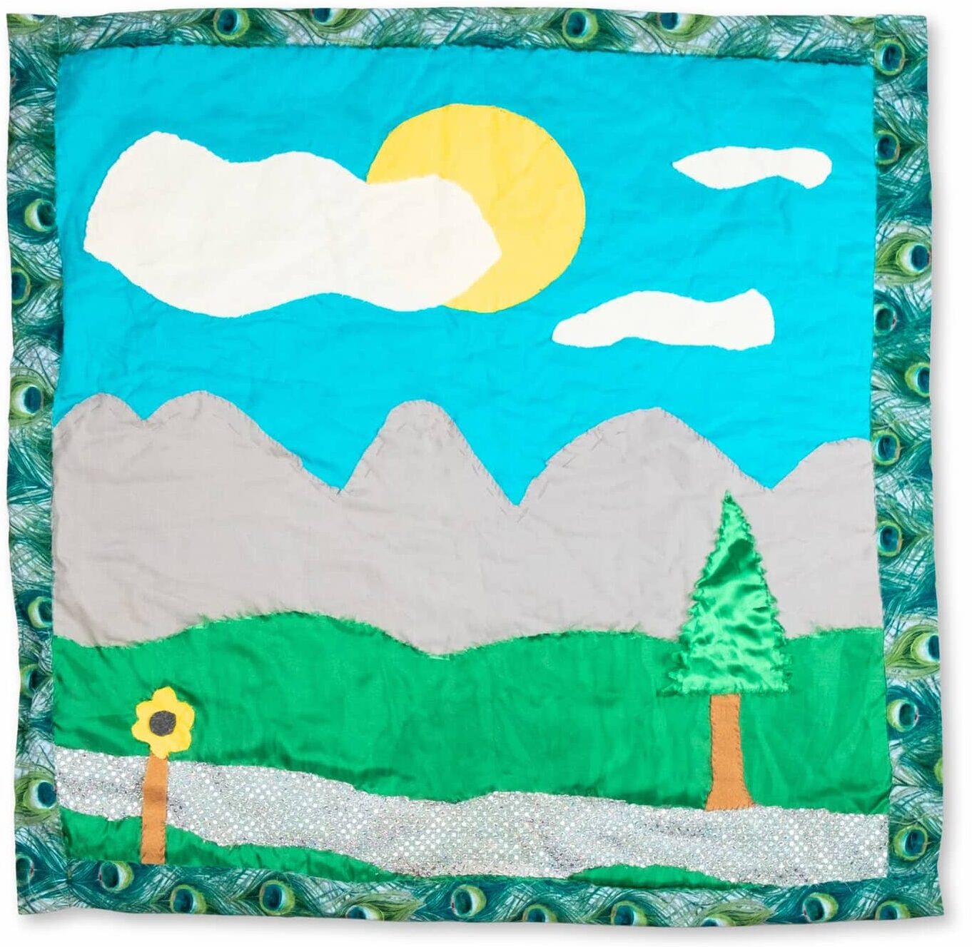 A quilt depicting a green field, mountains, and a sunny sky.