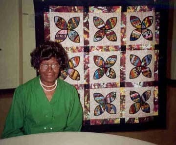 Viola Williams Canady posing in front of a nine-block quilt. 

