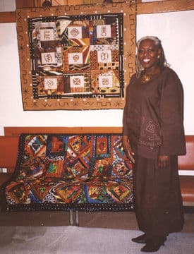 Donnette Cooper posing in front of a nine-block quilt.