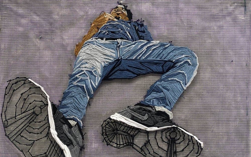 A worm’s-eye-view embroidered portrait looking up at a man wearing Nike sneakers, blue jeans, and a blue shirt.
