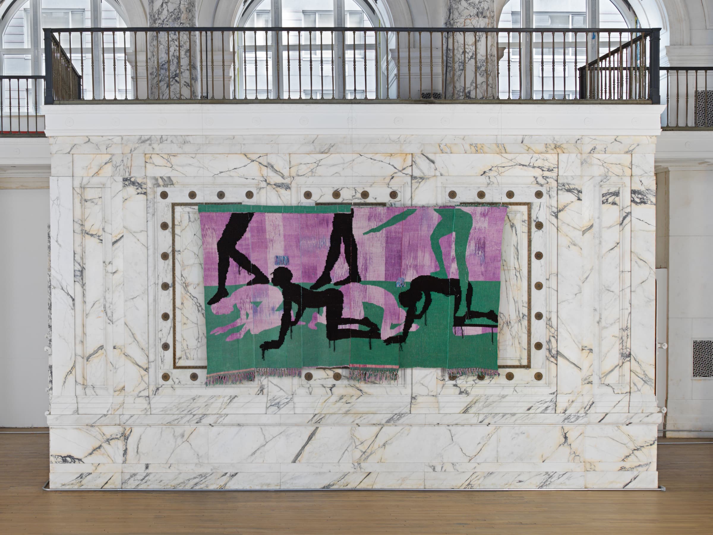 A green, purple, and black weaving of bodies crawling on the floor and others walking over them.
