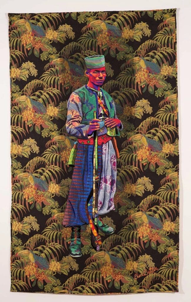 Quilted portrait of a Black Zouave soldier in a brightly patterned uniform against a background of colorful ferns. Bisa Butler, Zouave. 
