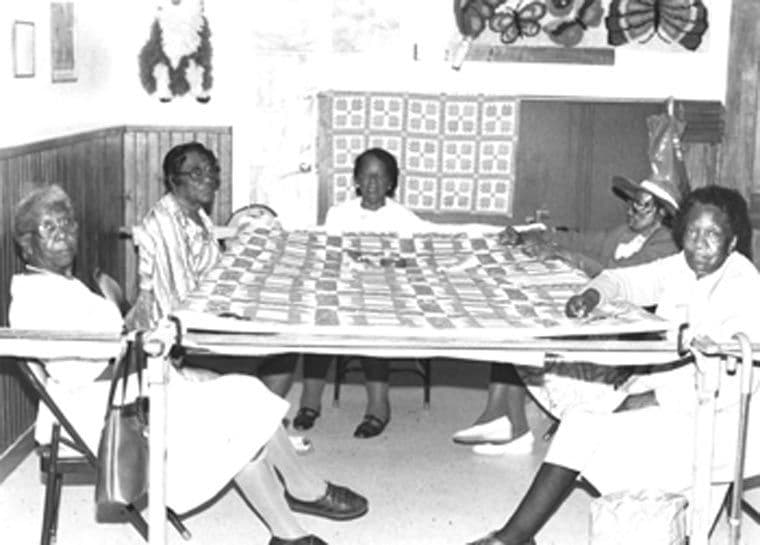 Participants in the Lake Providence Senior Citizen Center Quilting Bee in Louisiana, 1993, seated around a quilt.