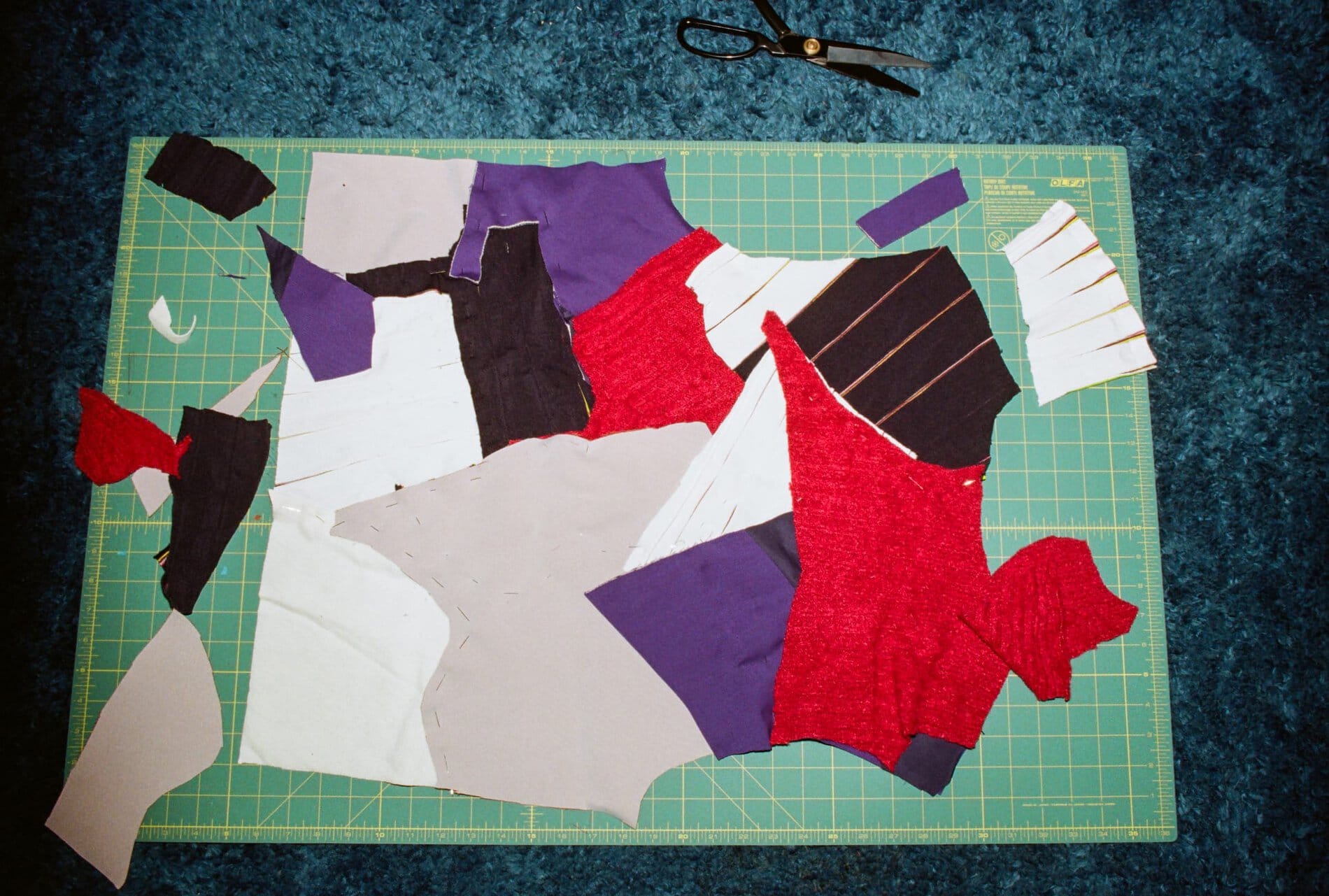 Red, purple, white, and brown fabrics laid on top of each other on a cutting mat.

