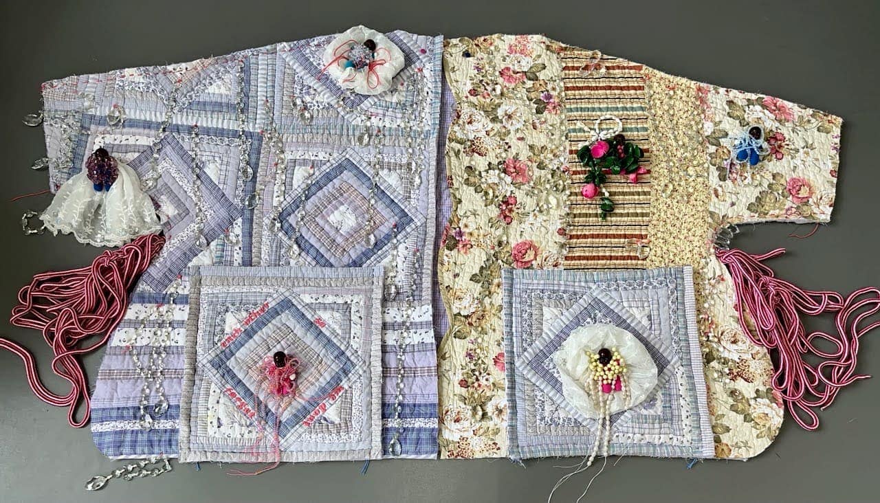 A quilted top of blue geometric and beige floral fabrics with three-dimensional embellishments.
