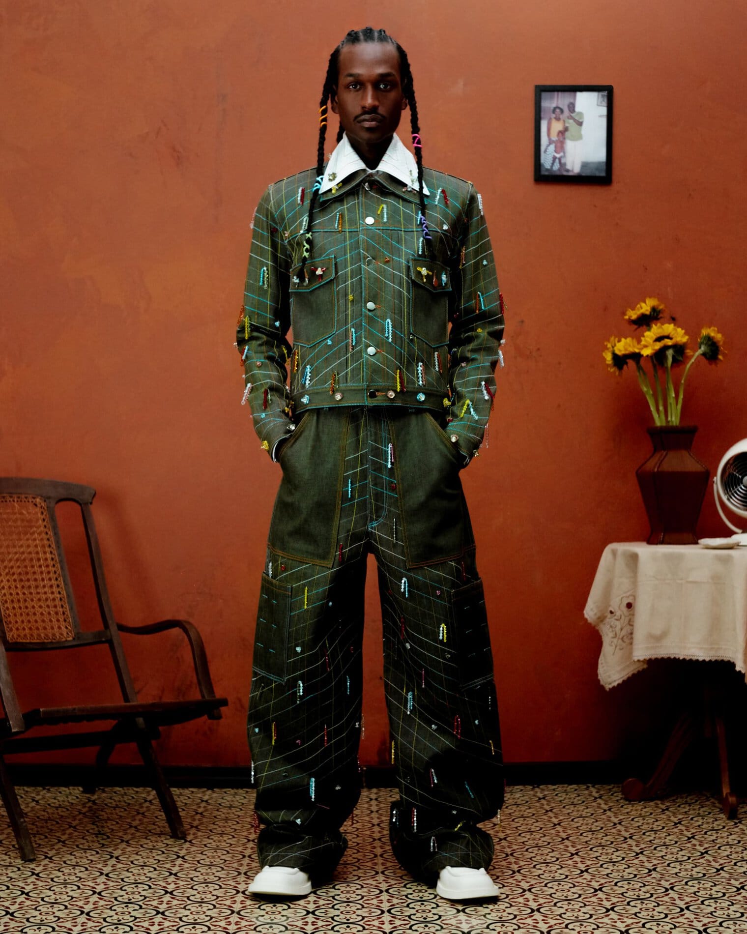 A model poses in a two-piece green denim jacket and pants set decorated with beads.
