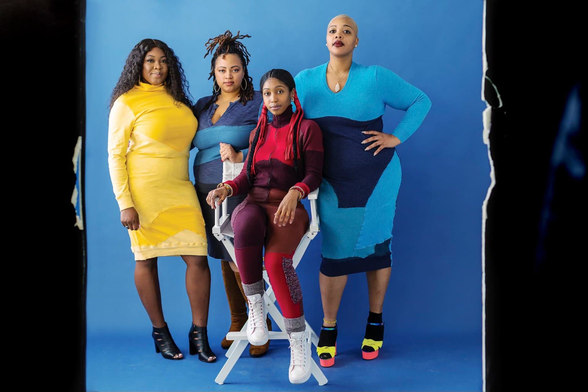 Four women posing together, modeling clothing designs.
