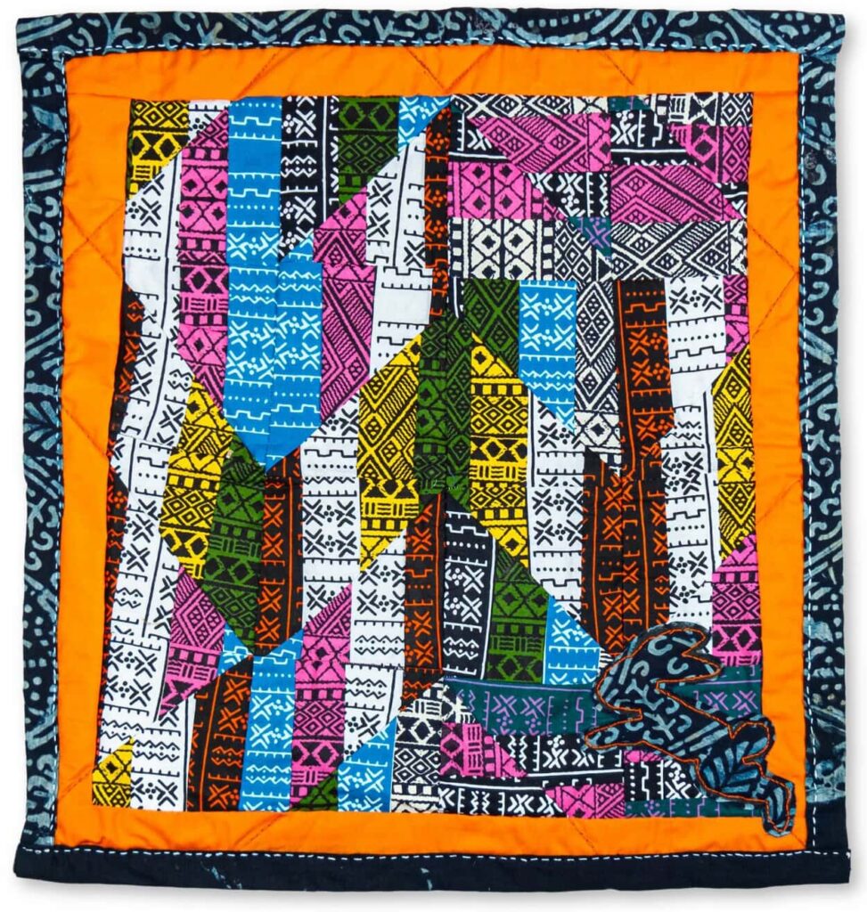 A quilt with blue patterned and orange borders featuring a blue bunny in the lower right corner and a stripped chevron pattern of many colored fabrics across the face of the quilt (front and back).