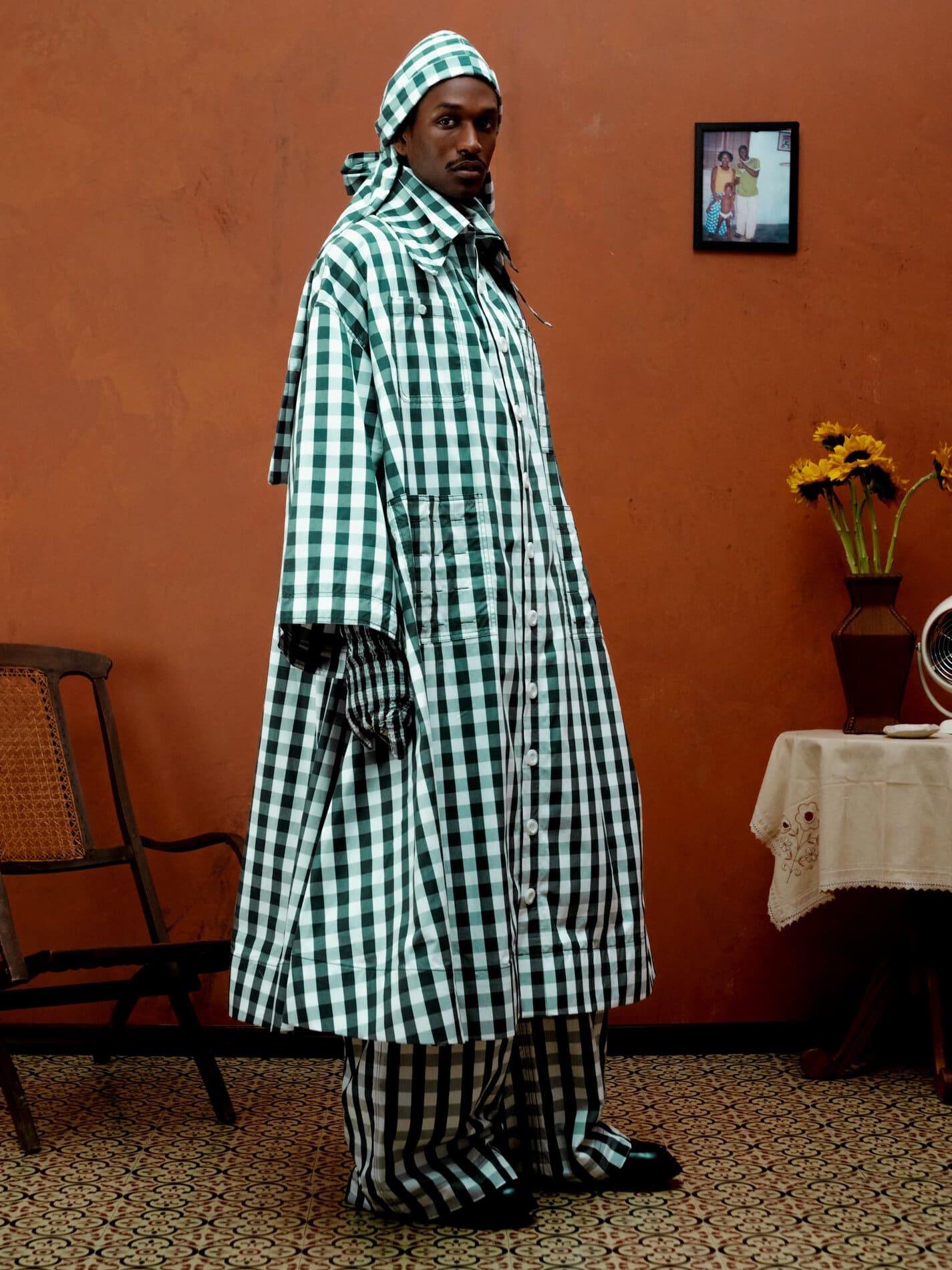 A model poses in a calf-length green and white gingham a-line jacket, and gloves, pants and headwear in a matching pattern.