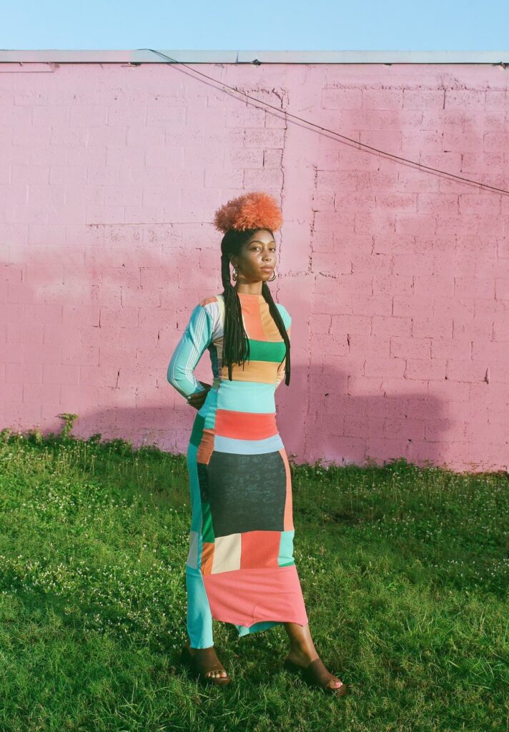 A woman in a colorful, tight long-sleeved dress posing outside.
